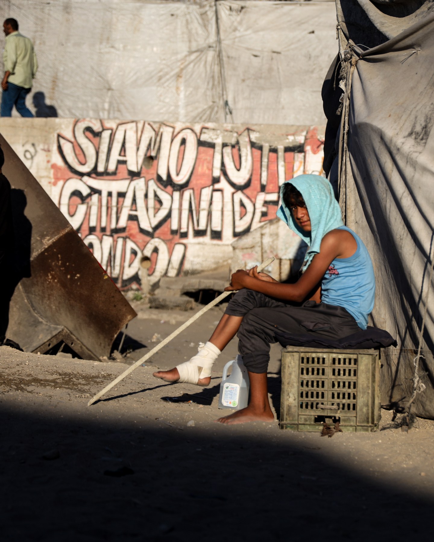 Una persona seduta davanti a una scritta su un muro, in una fotografia del progetto.